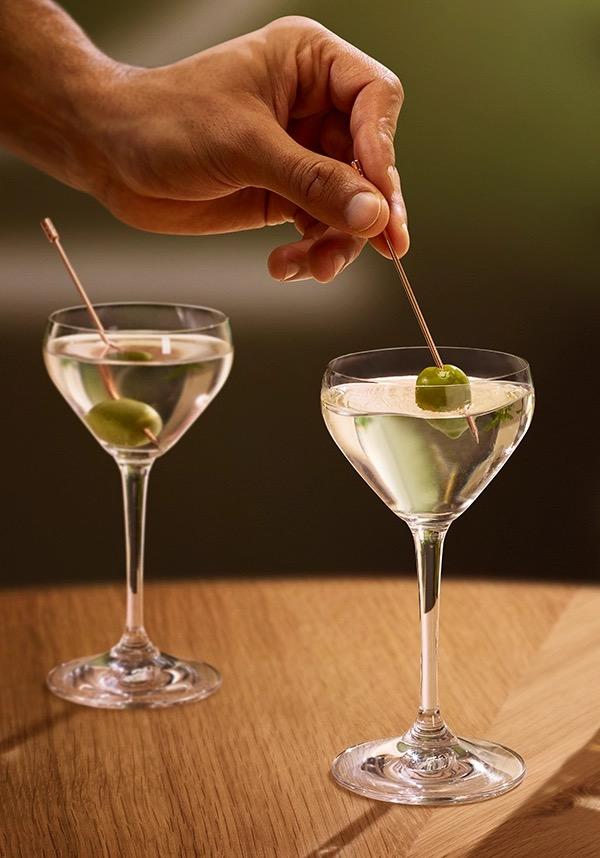 Ketel One Dirty Martini in Nick and Nora Glass with hand adding olive