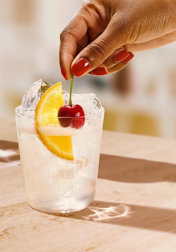 Ketel One Vodka Collins in Rocks Glass with hand adding cherry
