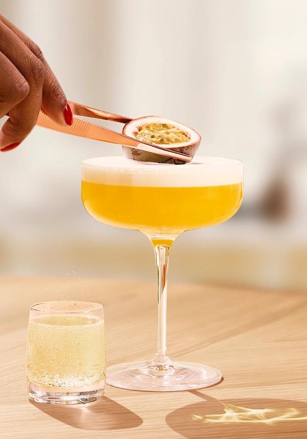Ketel One Passion Fruit Martini in Coupe Glass with hand adding passion fruit 
