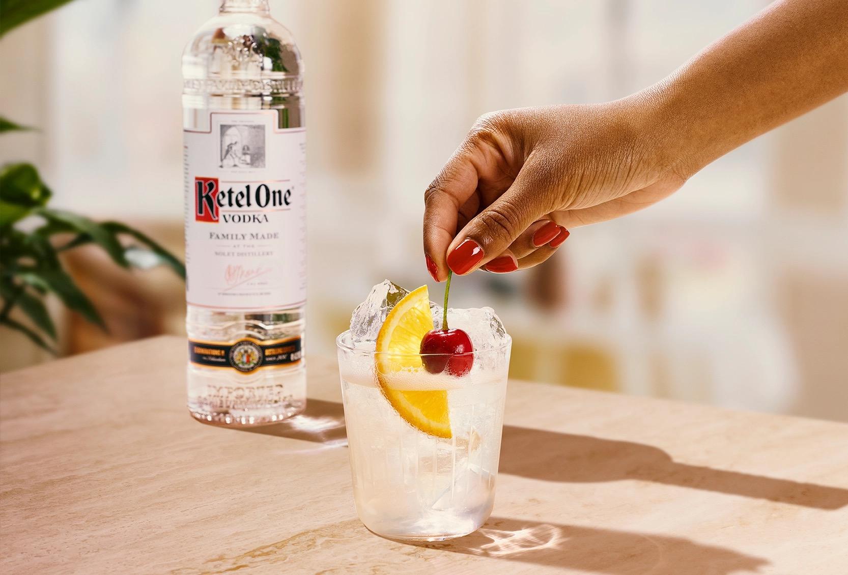 Ketel One Vodka Collins in Rocks Glass with hand adding cherry