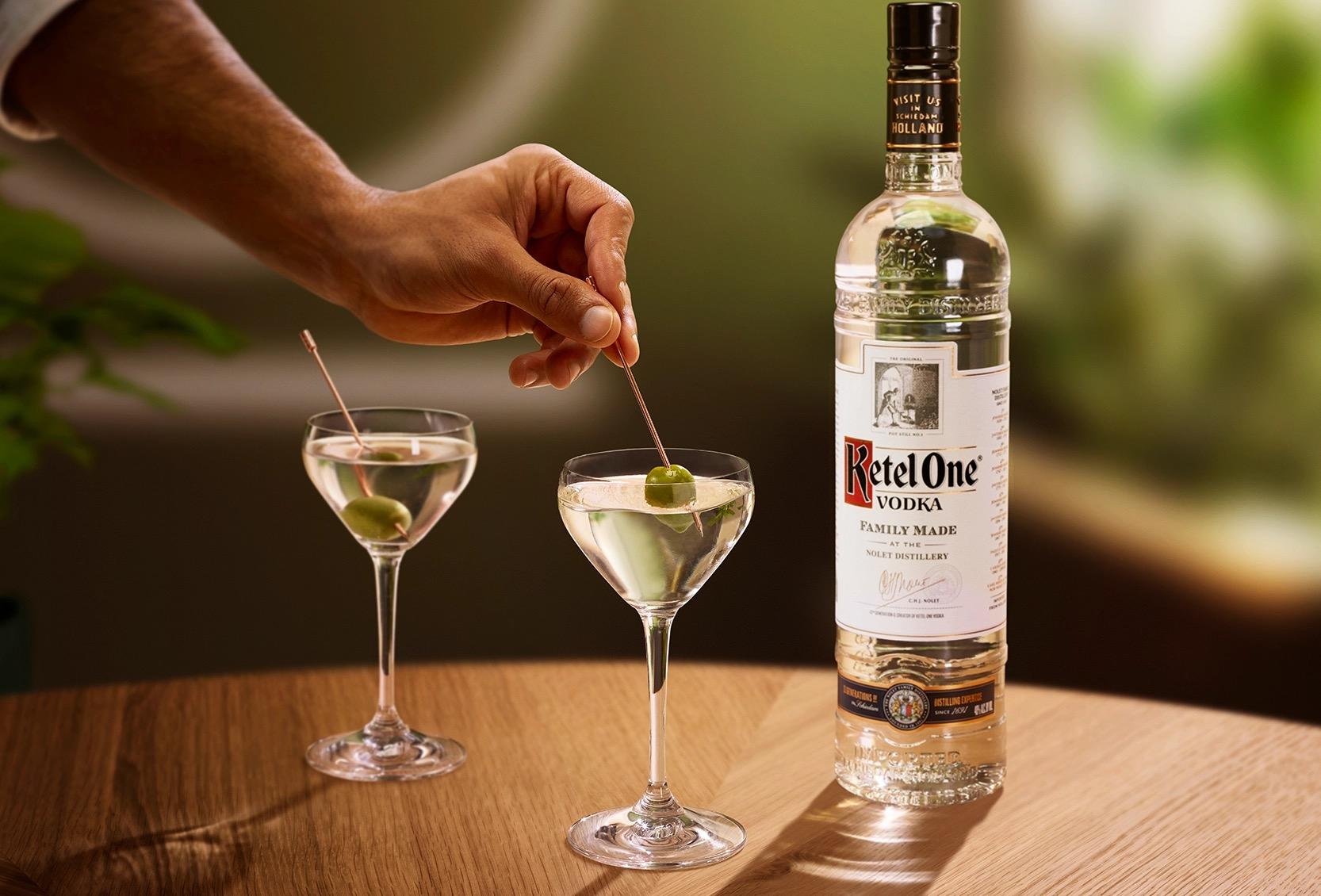 Ketel One Dirty Martini in Nick and Nora Glass with hand adding olive